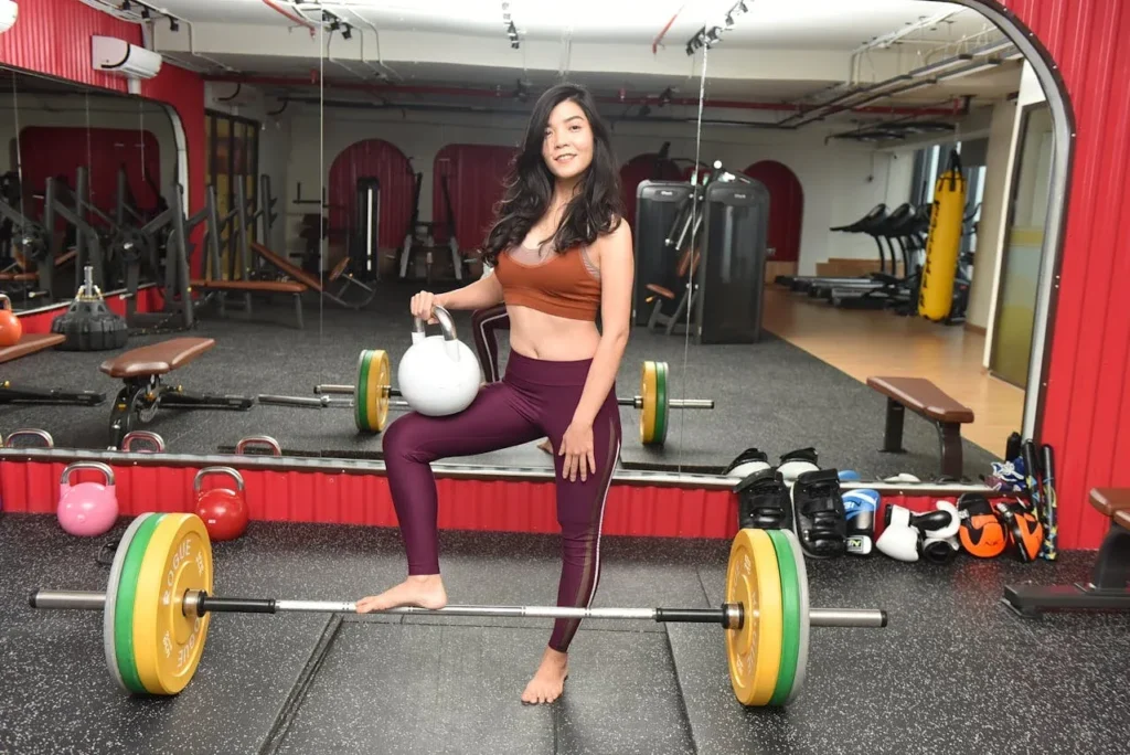 Strength Training Tips for Women: 10 Essential Strategies to Transform Your Fitness 9 woman standing in gym with kettlebell in hand and barebell at her feet