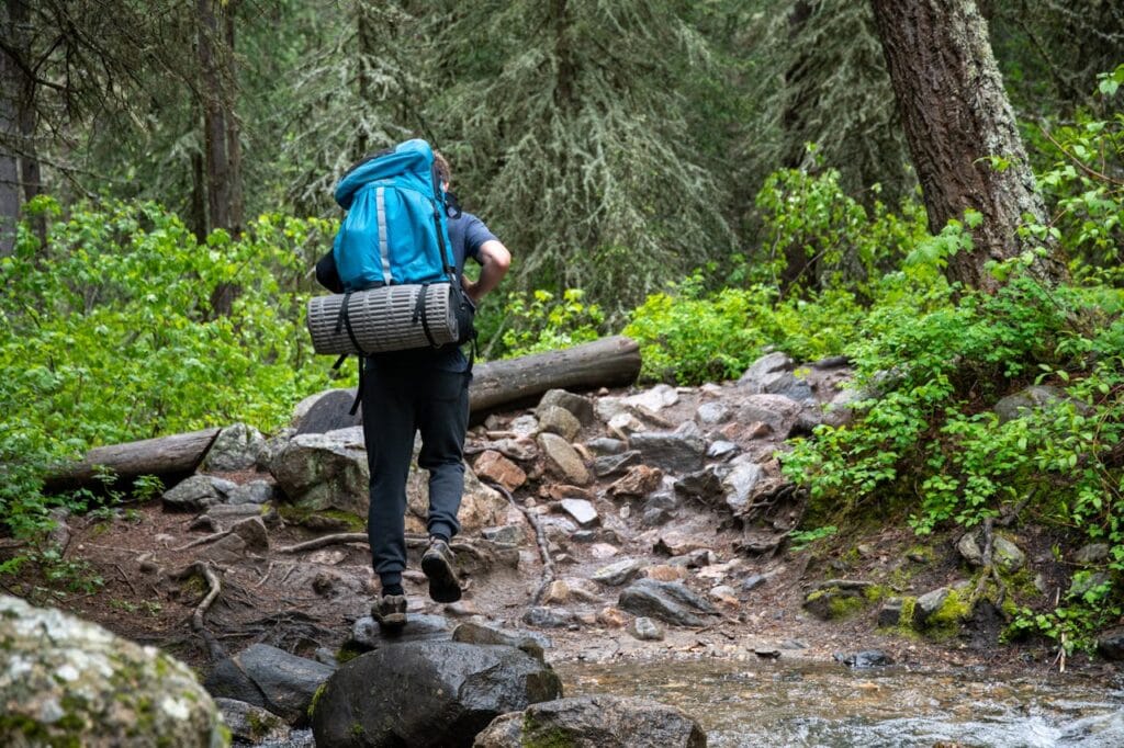 7 Powerful Fitness Tips for Van Life: Stay Fit with Bodyweight Training for the Road 4 man with heavy pack moving across rocky ground into a forest