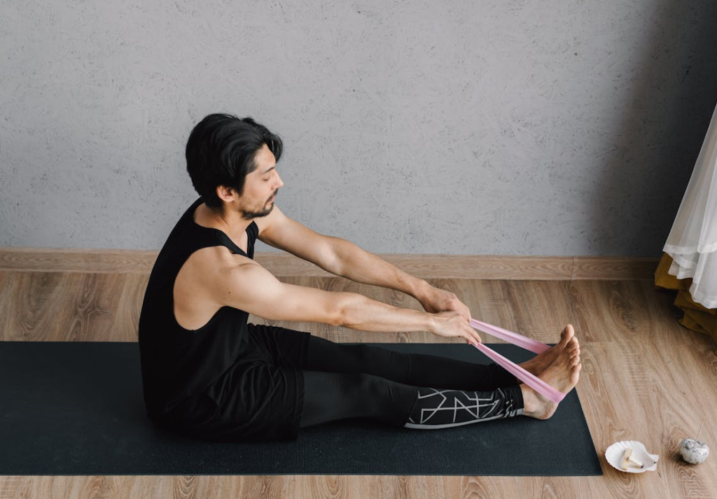 7 Powerful Hotel Workouts Without Equipment to Keep You Fit on the Go! 10 man using bands for stretching out calves while sitting on a yoga mat
