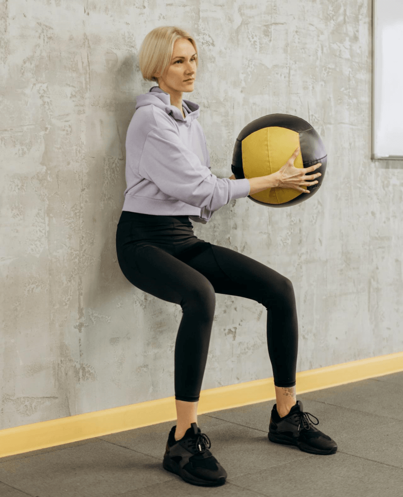 7 Powerful Leg Exercises Without Weights for Ultimate Strength 8 woman doing wall sits with a medicine ball