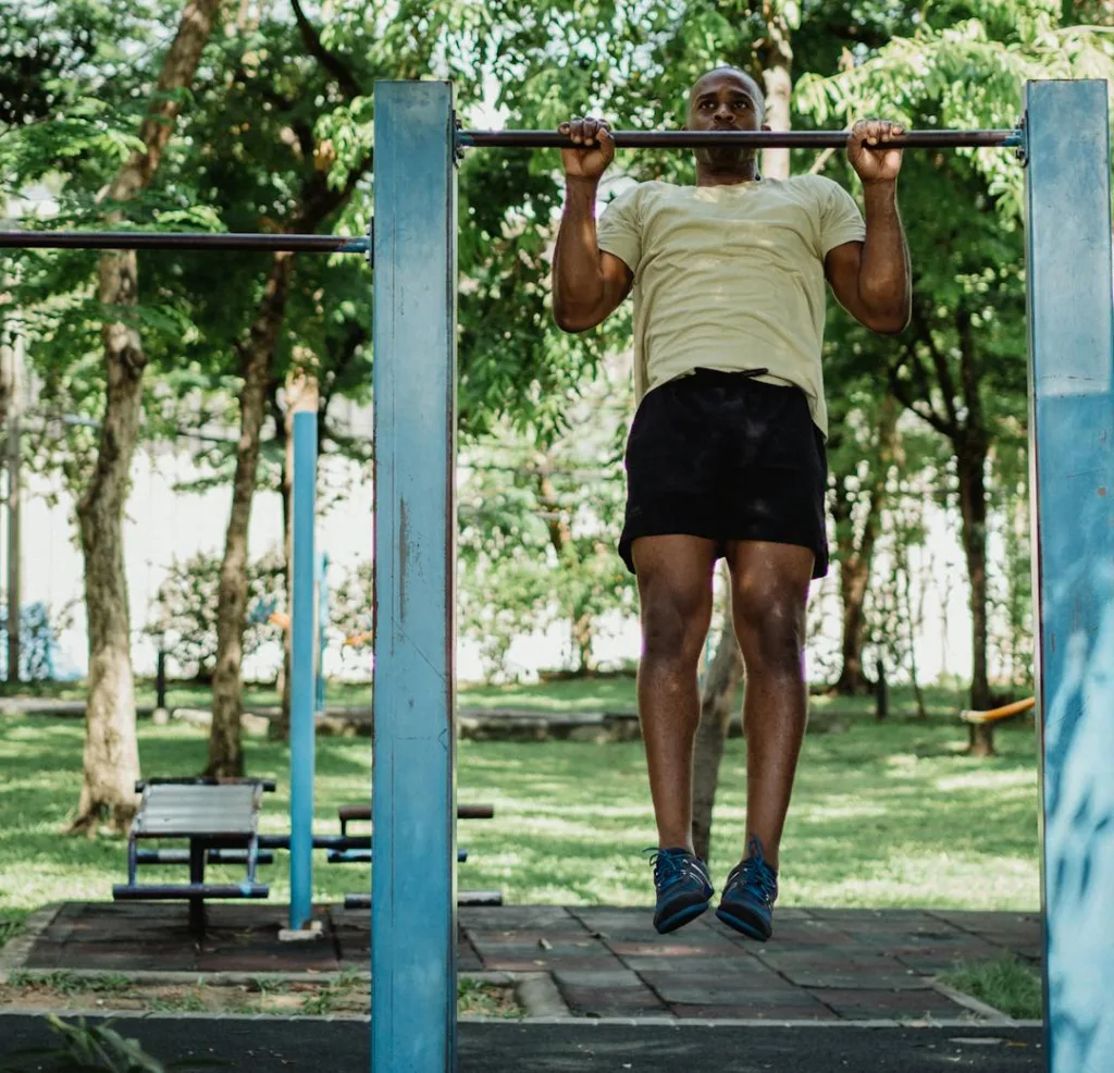 man performing pull-ups in a park on a summer day
