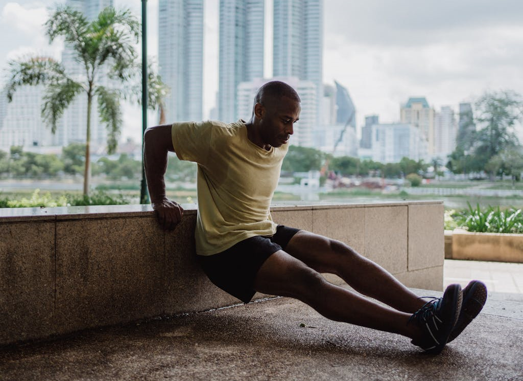 7 Powerful Hotel Workouts Without Equipment to Keep You Fit on the Go! 7 man doing triceps dips outside of hotel with scenic tropical trees and a city in background