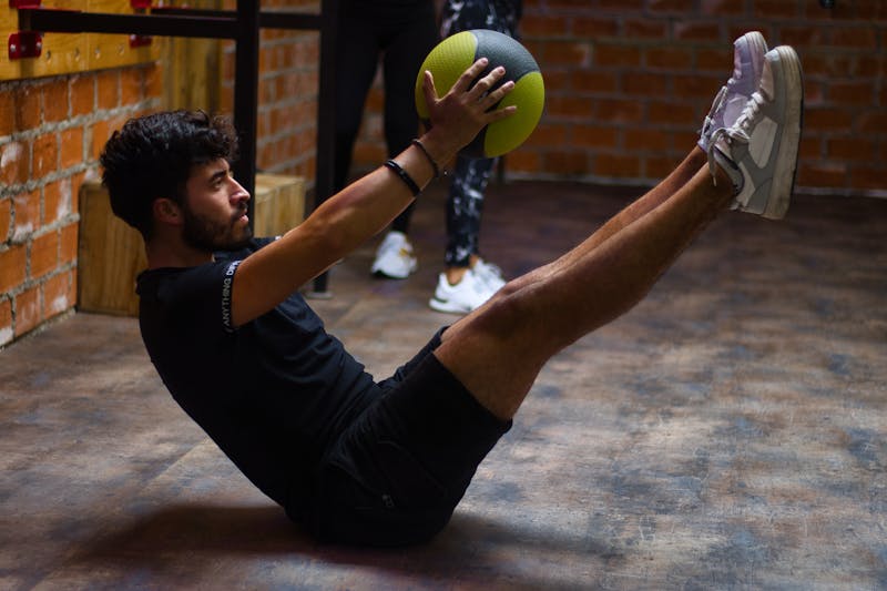 Ultimate Guide: 7 Ways to Combine Calisthenics and Yoga for Full-Body Fitness 5 a man performing a version of yoga boat pose but using a weighted ball to increase difficulty