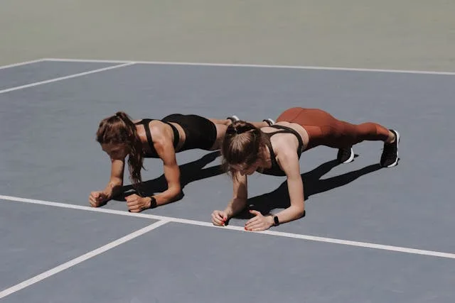 two women demonstrating a plank hold on elbows outside