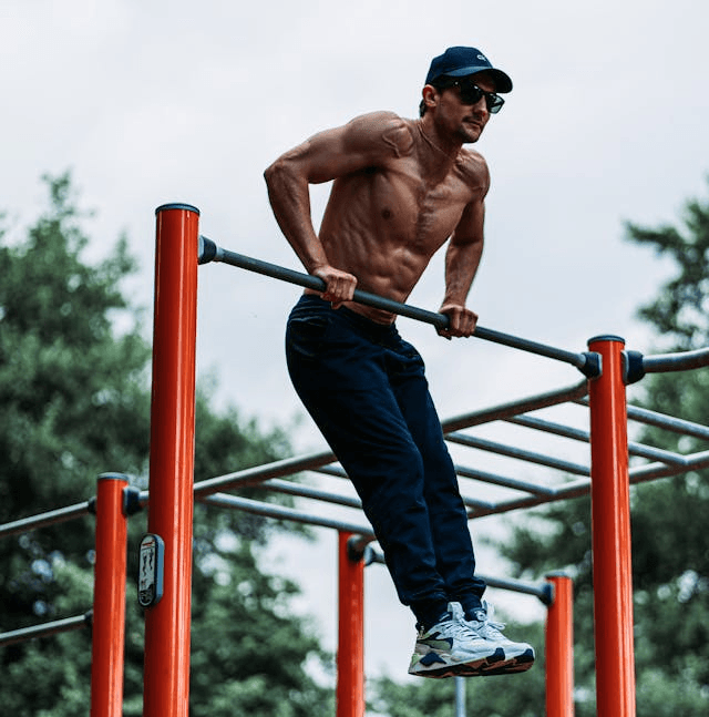 No Weight Workout: The Best Full-Body Routine and Gear to Take It to the Next Level 3 man demonstrating an upper portion of a muscle up on a bar outside in an exercise park