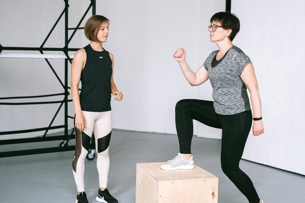 Unlock Strength and Longevity with These 5 Senior Fitness Workouts 4 image of an older woman performing a step up while her trainer observes