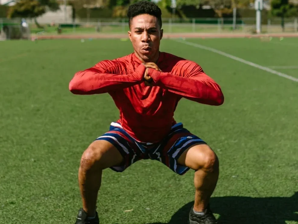 10 Simple Home Workouts for Beginners to Boost Fitness and Strength! 3 man doing air squats outdoors in a grassy field