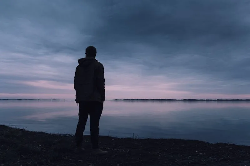 man looking out over a dark sky and lake