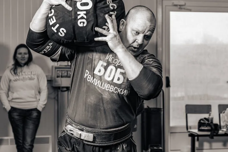 strongman hoisting a heavy sandbag on his shoulder