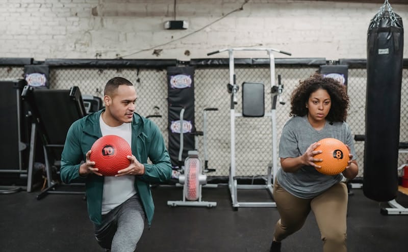 7 Powerful Functional Fitness Moves for Tough Times 7 man and woman doing lunges while holding weighted medicine balls