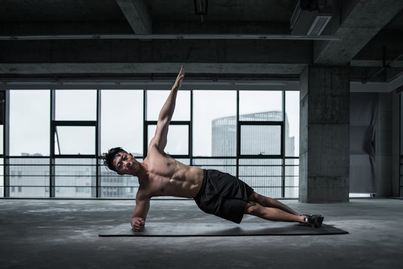 Functional Strength Through Calisthenics: Unlocking Your Full Potential 4 man performing side elbow plank in open studio