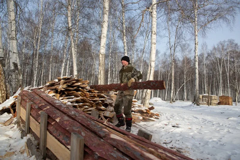 man carrying hand hewn lumber in a winter climate