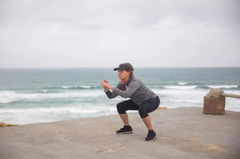woman performing air squats beach side